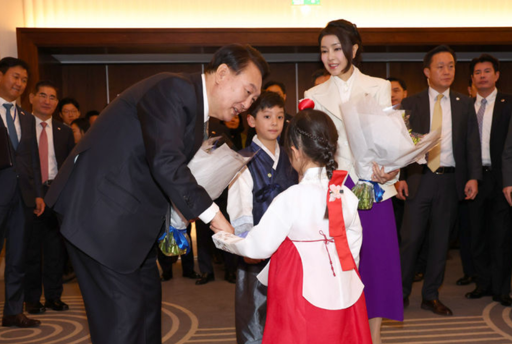 韩国夫人抵达英国第一个活动，出席韩国同胞会，穿白色西服配紫裙，一身撞色打扮牵着小