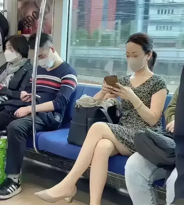 在地铁车厢里，一名女子穿着精致，专注于她的手机屏幕。她身着时髦的连衣短裙，裙摆轻