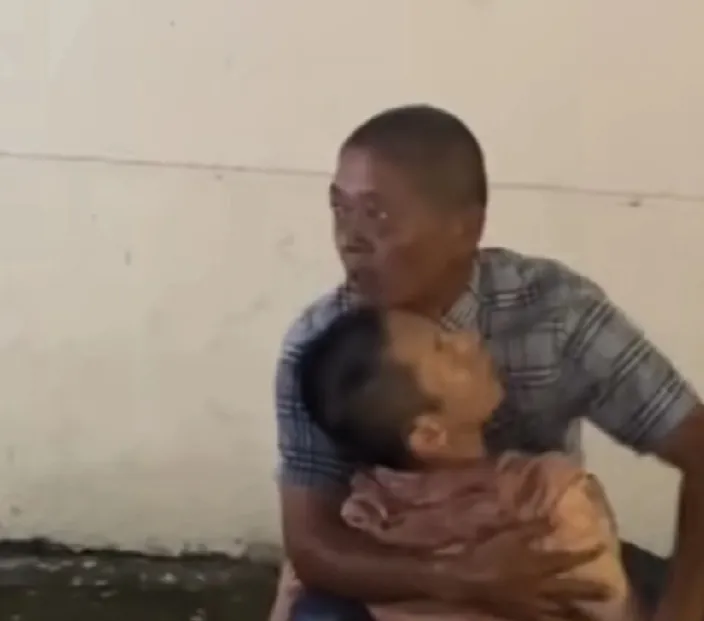 父亲一脸迷茫，怀里搂着他喝酒喝死的儿子。视频拍摄者说这位父亲赶到时他儿子已经不省