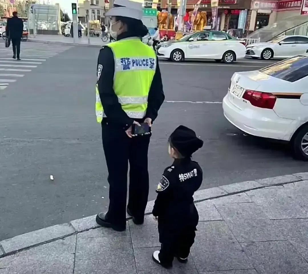带着孩子上街执勤，不妥！
这张照片，说的是，一位女警察，带着自己的小孩，站在路边