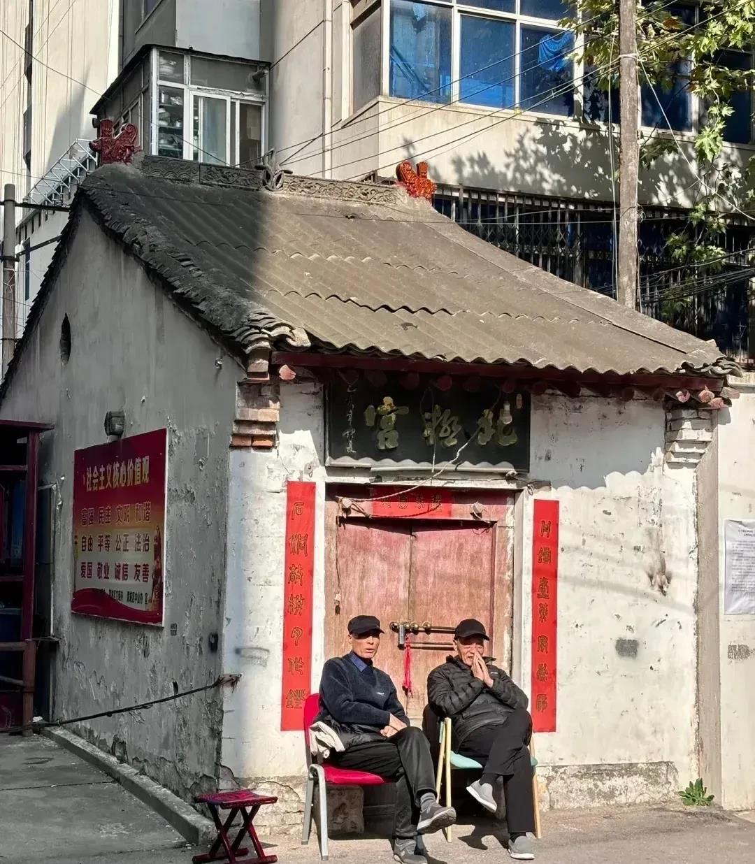 两位老人晒太阳的地方不简单，后面的破旧房子上面有一块匾，上写“北极宫”，里面应该