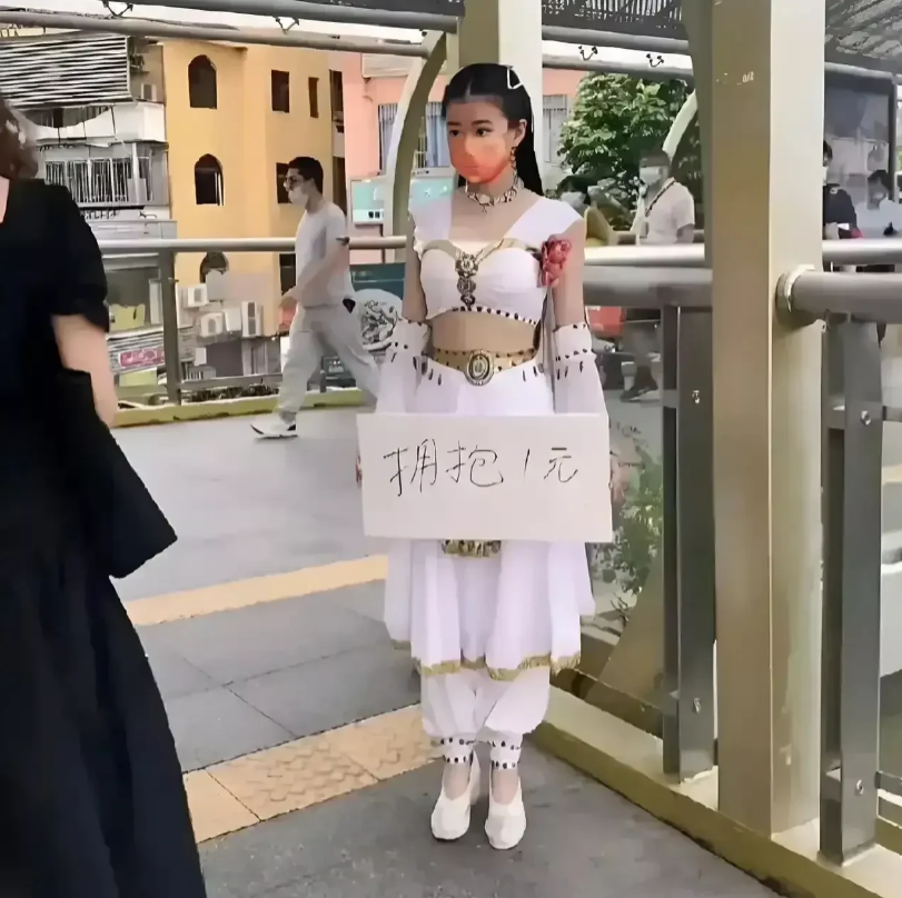 广东深圳，在龙岗区丹竹头附近，一名年轻的女子站在天桥上举牌，牌子上写着一元拥抱，