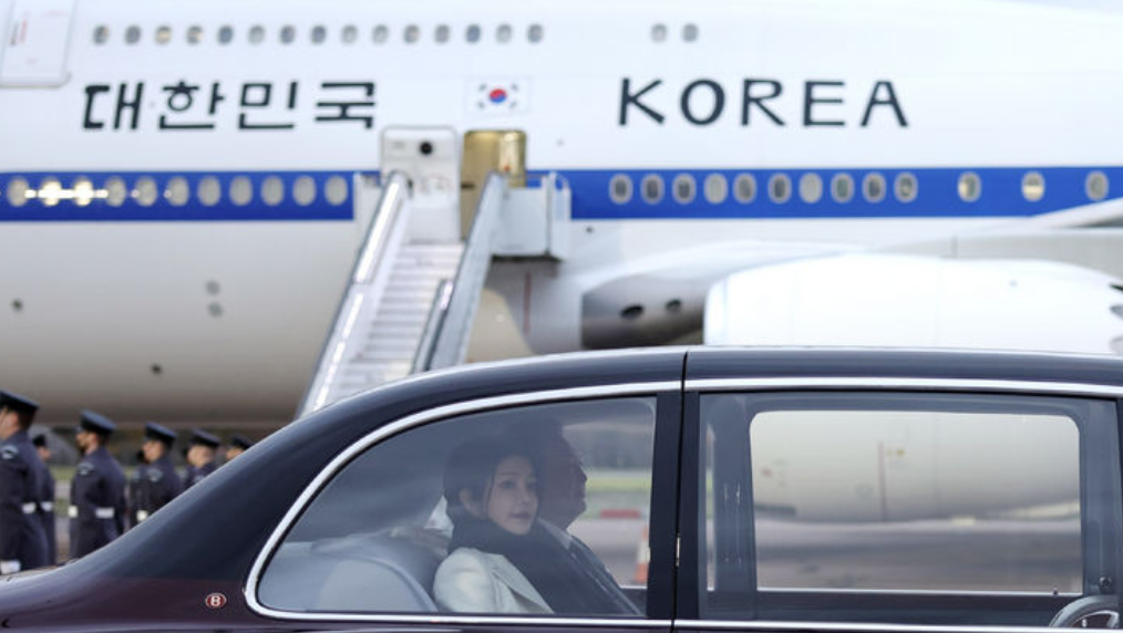韩国夫人和老公抵达英国，还是出发时的服装，只是把黑色围巾塞进了白色西服里，一身黑