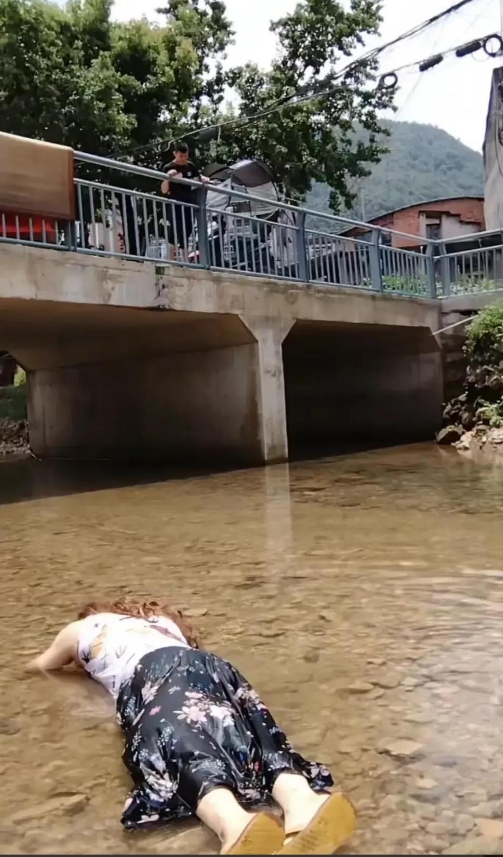 在一条水深仅过掌心的小河里，一名女子俯身躺着。桥面上站着一名男子。这一场景引发了