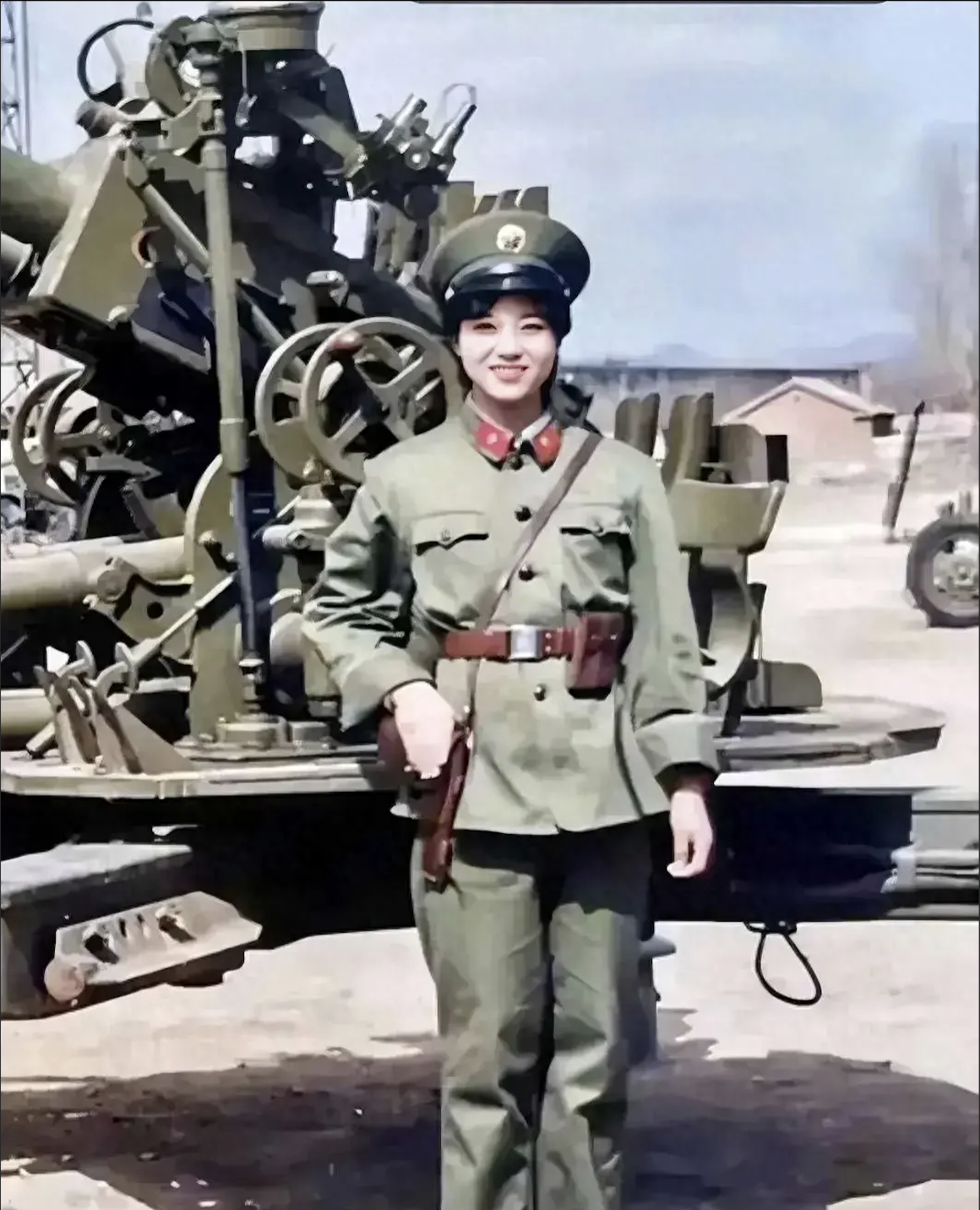 八十年代，一位女兵身穿绿军装，头戴大盖帽，身姿挺拔，傲然而立

她站在高射炮前，