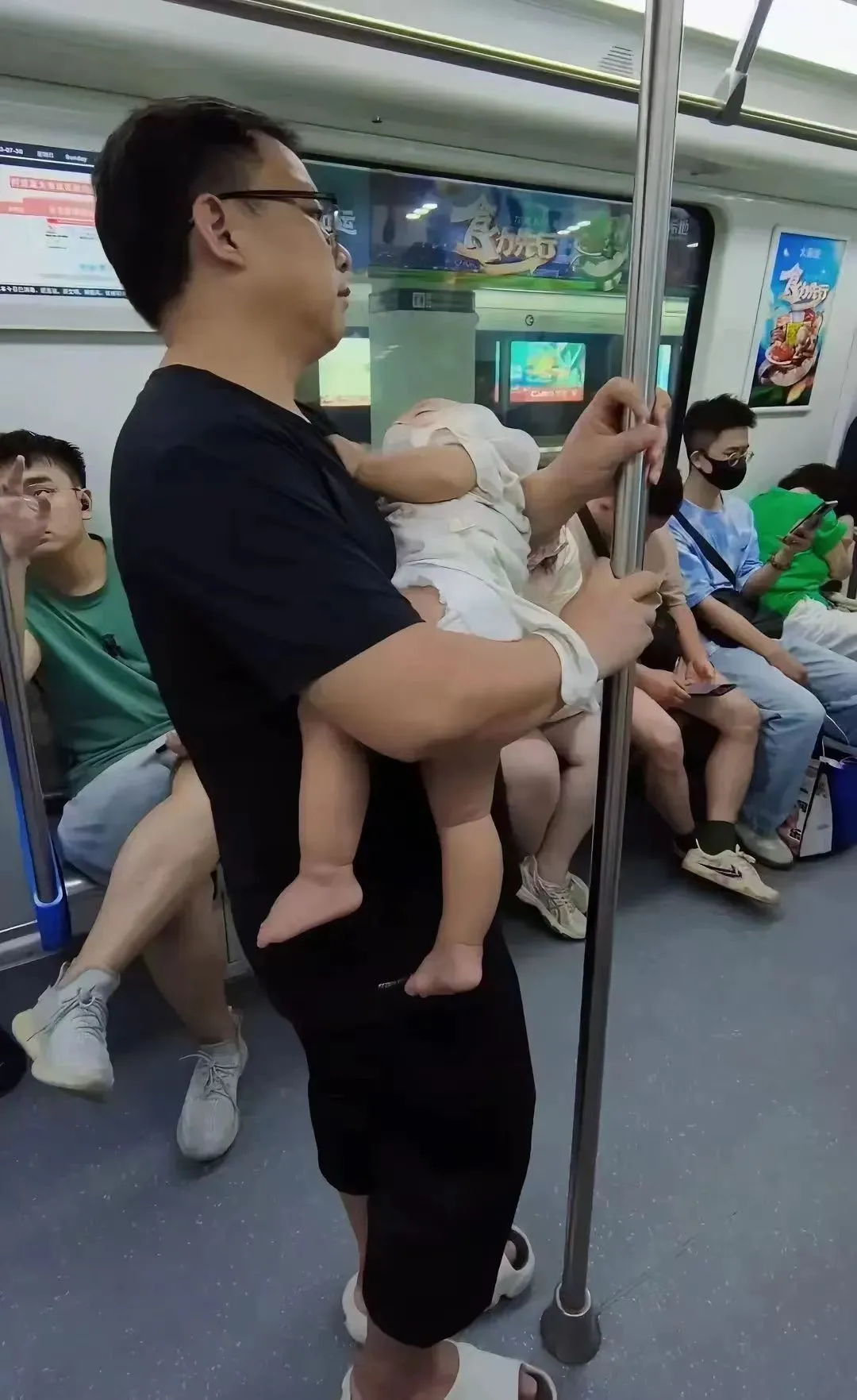 一段令人痛心的视频中，一位男子抱着沉睡的小孩，双手紧紧抓住杆杆，生怕小孩掉落车厢