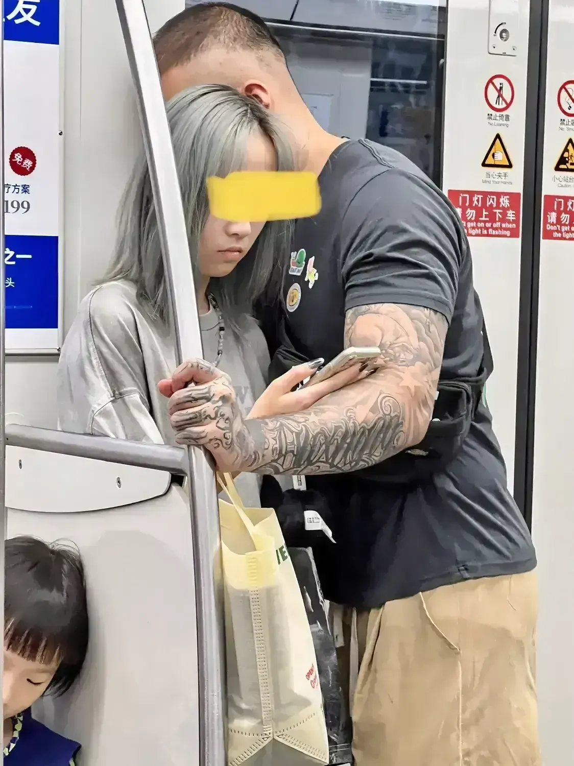 在地铁车厢内,一个看上去非常稚嫩感觉像16岁左右的少女，被一个强壮的花臂男搂着。