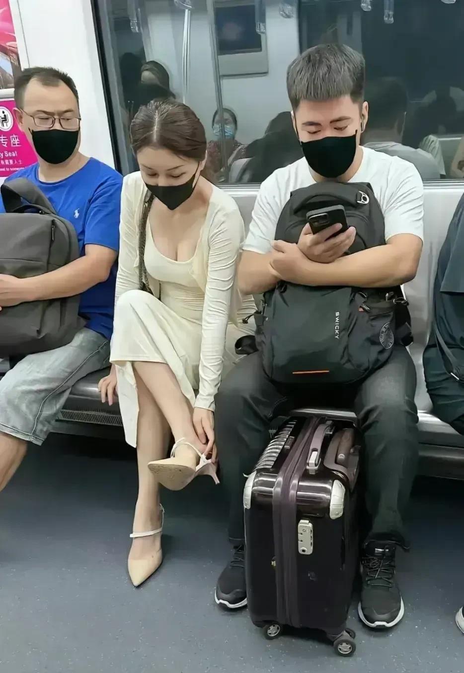 图片中的场景，是地铁车厢里的一组乘客乘车的一景。一位白衣女子的左右两侧分别坐着两