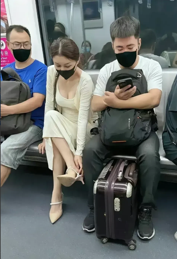 图片中的场景，是地铁车厢里的一组乘客乘车的一景。一位白衣女子的左右两侧分别坐着两