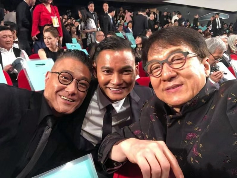 托尼贾和成龙罕见同框出镜，曝光的画面中成龙戴着眼镜留着刘海看起来状态超好，而罕见