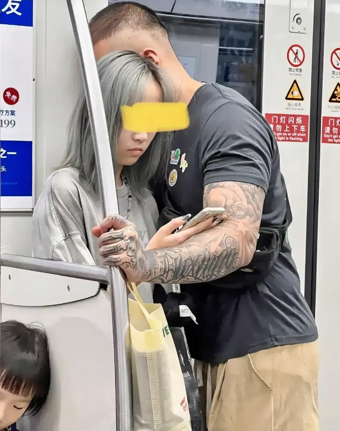 地铁里，一个看上去十分稚气的16岁左右的女孩，被一个花臂壮汉抱住。面对车上众人异