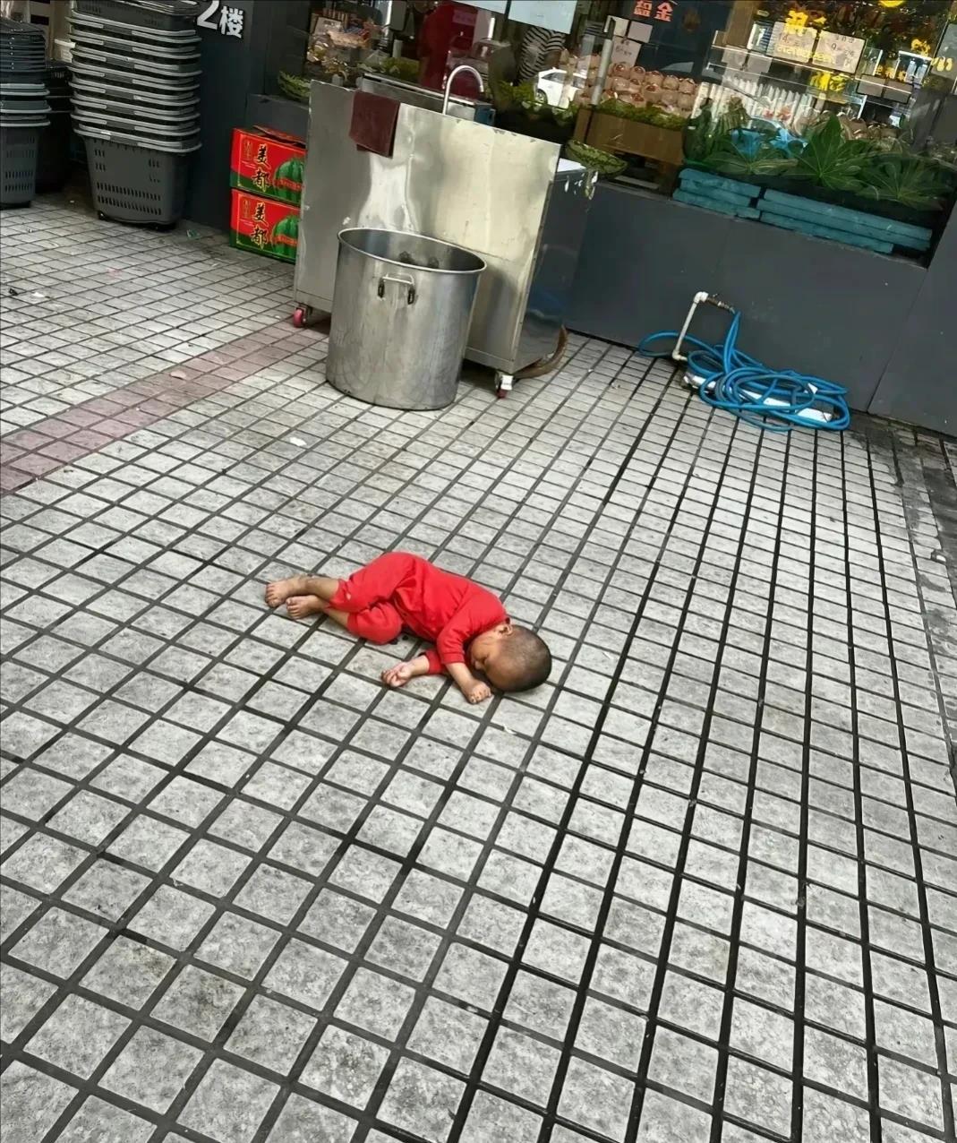 令人心痛的一幕发生在某水果店门口，一名幼童孤零零地躺在地上，吸引了周围路人的围观