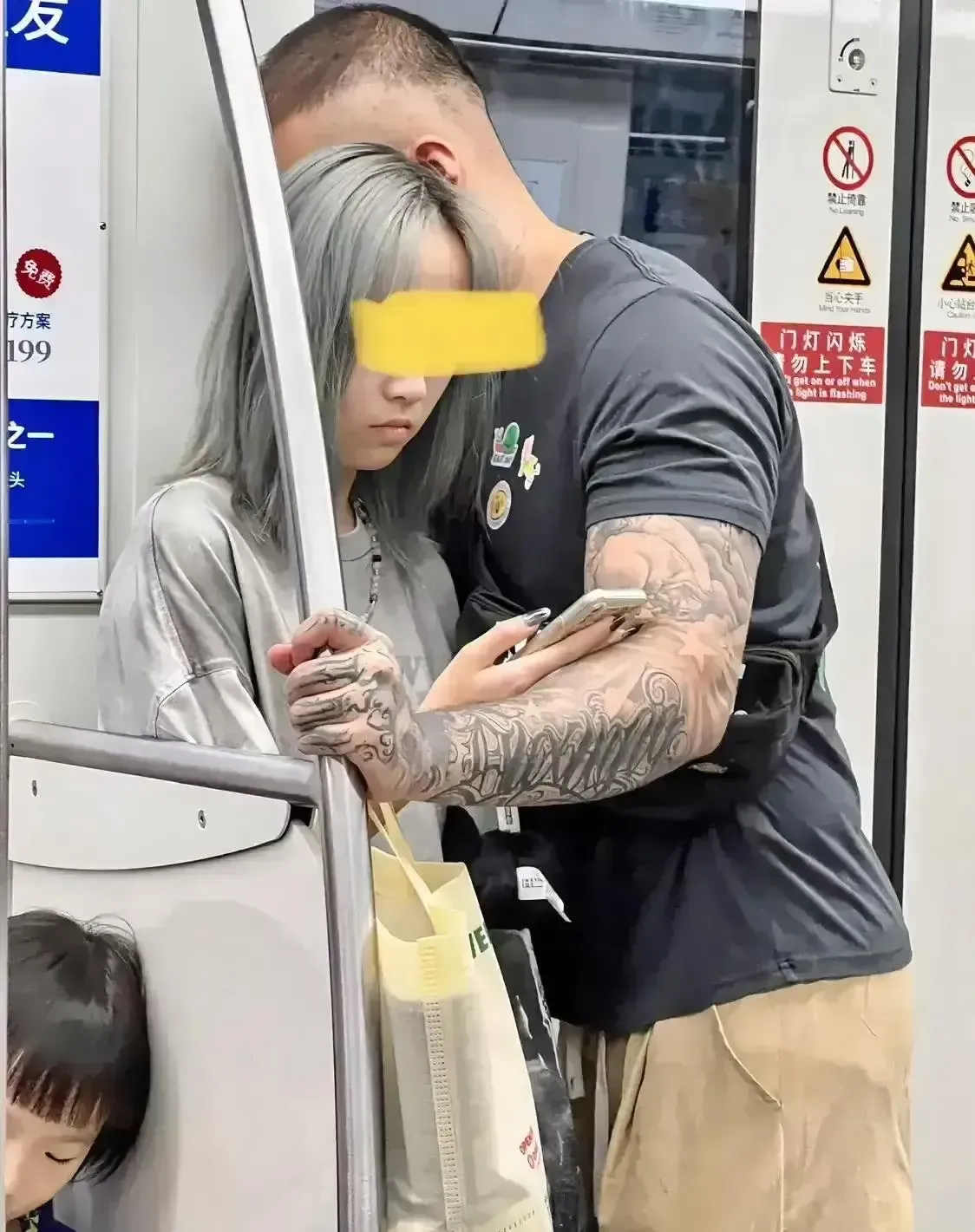 在地铁车厢内,一个看上去非常稚嫩感觉像十五六岁左右的少女，被一个强壮的花臂男搂着