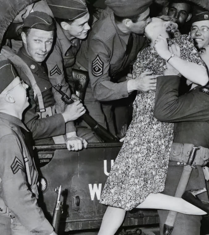 1940年，一名士兵举起一名年轻貌美的女人，将她送给卡车上的大兵，大兵见到女子不