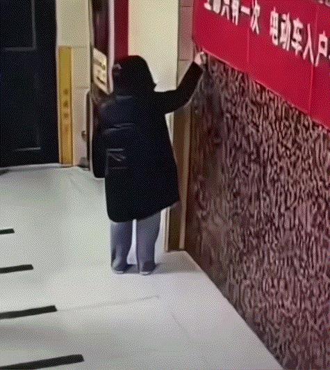 手太欠了！一女子走在居民楼内时，居然无缘无故的点燃了挂在墙上的红色横幅，且女子还