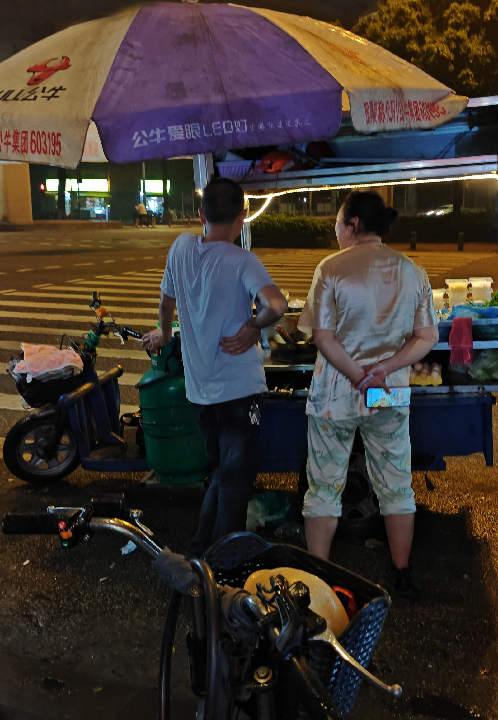 12点半，下起密密麻麻的细雨，夜市小贩撑起大伞，试图继续经营，但雨越来越大了。西