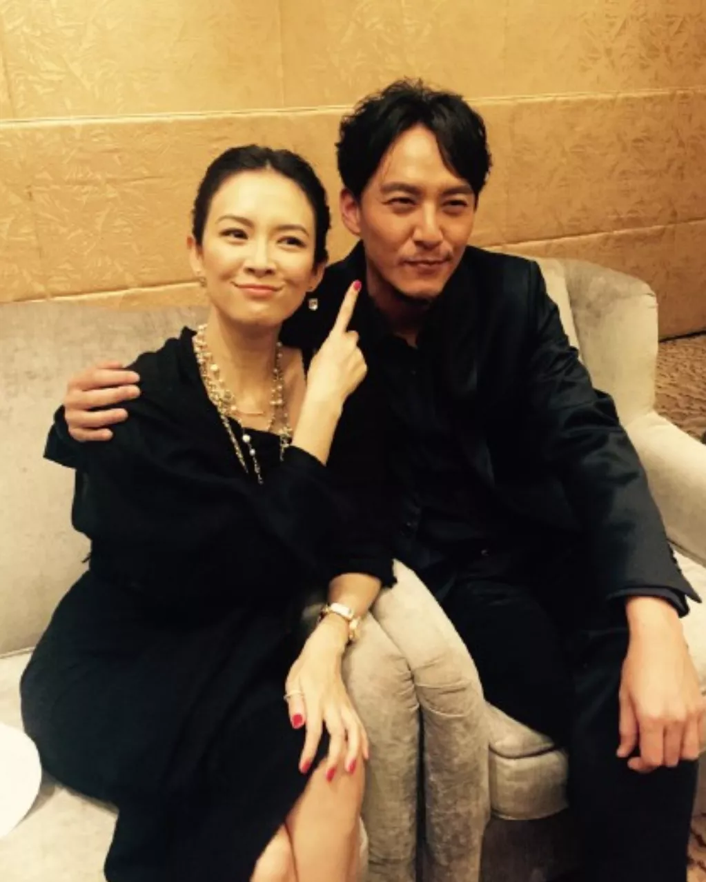 章子怡被身旁的帅气男士紧紧搂着，她用手指着身边的男子，脸上洋溢着调皮而又迷人的微