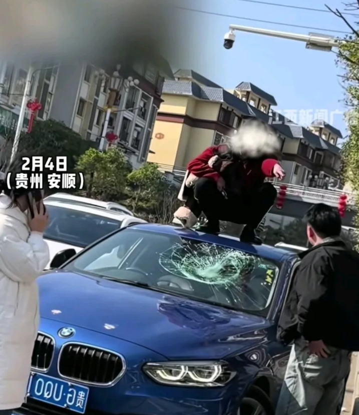 女子拦下宝马车，爬上车顶，愤怒地用脚踹碎车玻璃窗，而后蹲在车上指着老公说道：“我