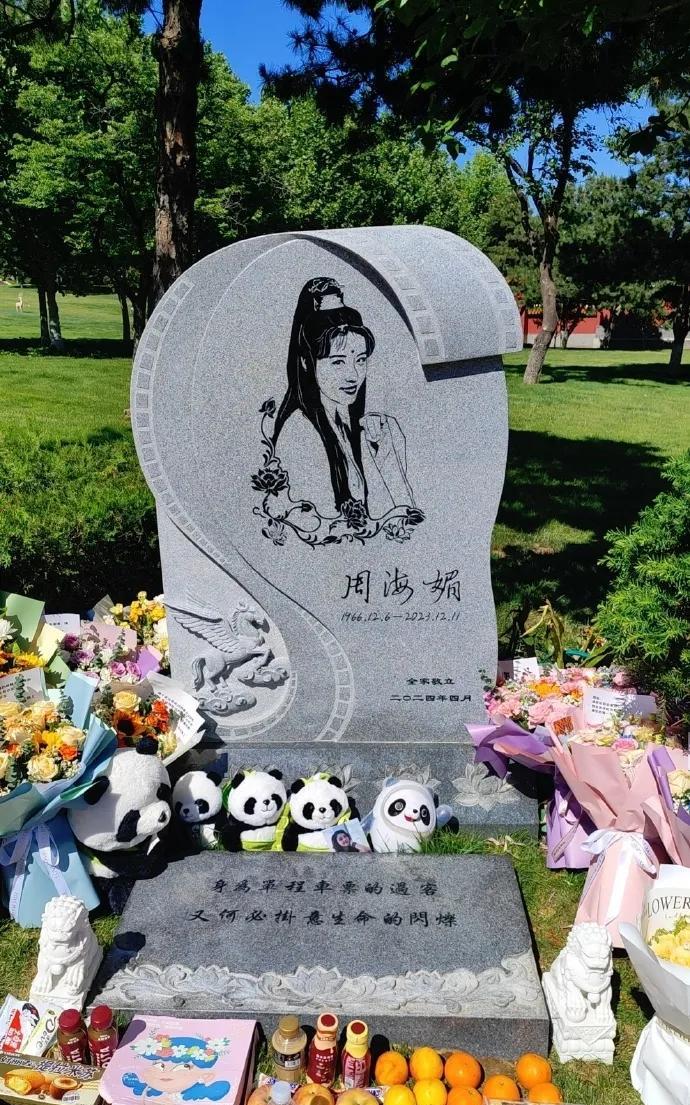 这是周海媚的墓地，在绿荫草地，鸟语花香，墓前摆满了粉丝们祭拜的各种水果，鲜花，贺