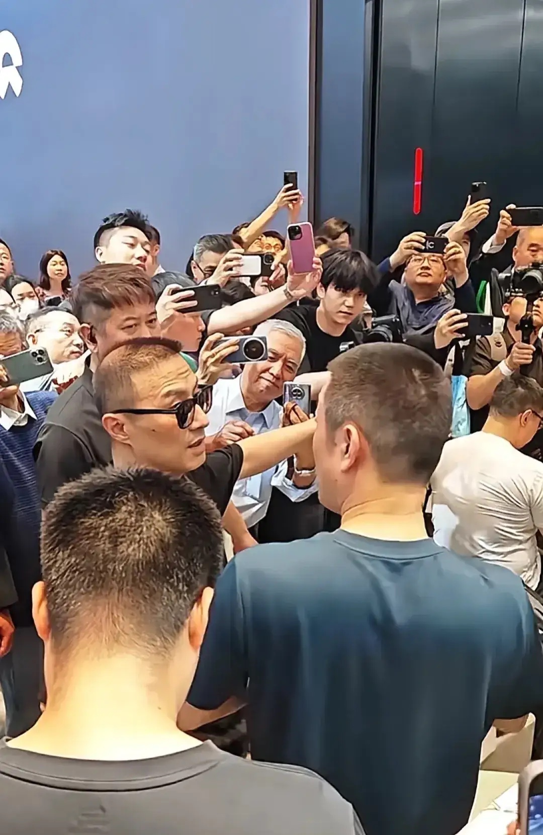 北京车展，蔚来李斌给歌手汪峰介绍新车，后面网友为了能无遮挡的拍到他两个，把手机举