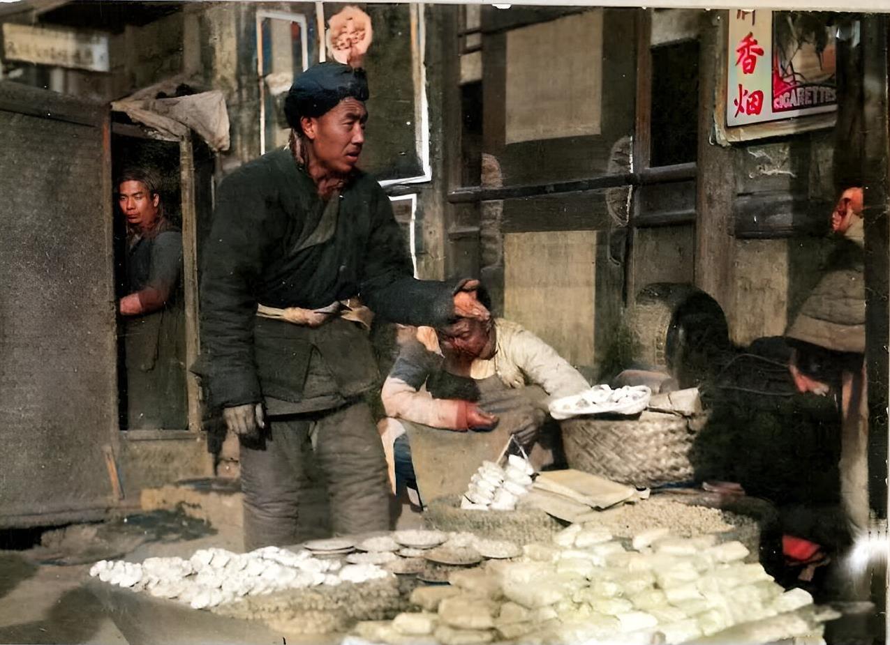 1920年代，北京一名小摊贩在商铺前的街上摆下小摊子。他的摊子上摆放着柿饼与花生