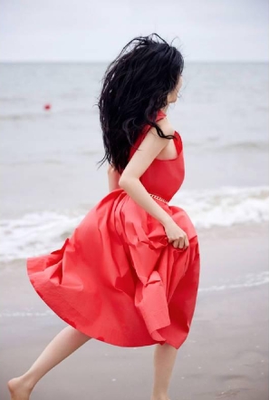 张俪穿红色长裙赤脚漫步海边，海风吹动长发回眸氛围感拉满。