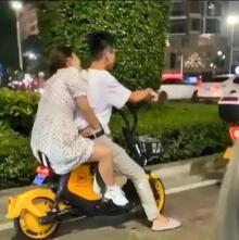 在繁忙的街道上，一位女孩坐在自行车后座上，竟然将手伸进了男孩的裤子里。这样的举动