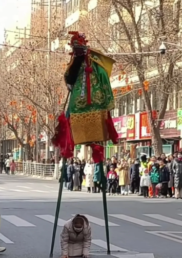 这是前几天在甘肃兰州游玩时，看当地社火时，拍下的一张照片，踩高跷，一路人跪在地上