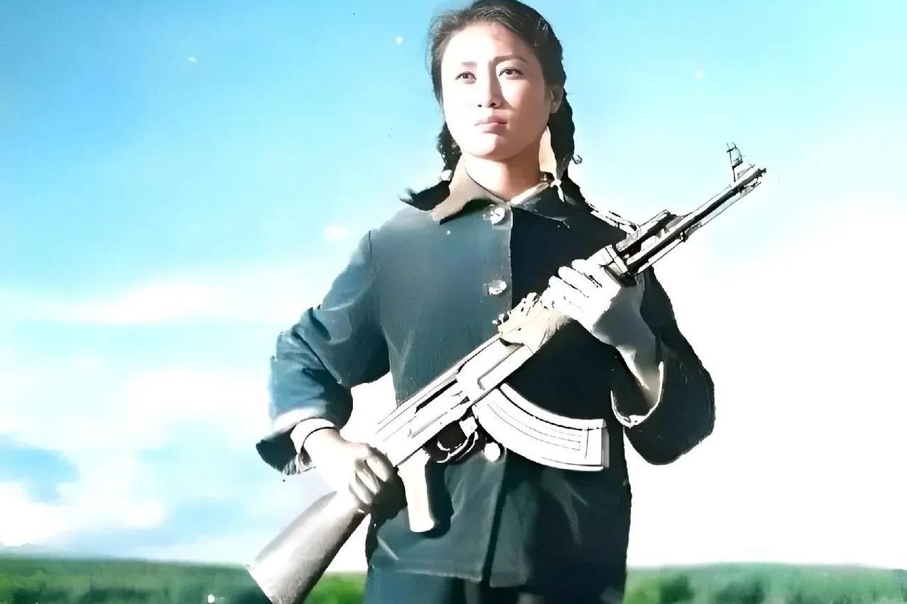 这是六十年代，一名女民兵在湖边的留影。只见她穿着灰蓝色的粗布衣裳，手持一把冲锋枪