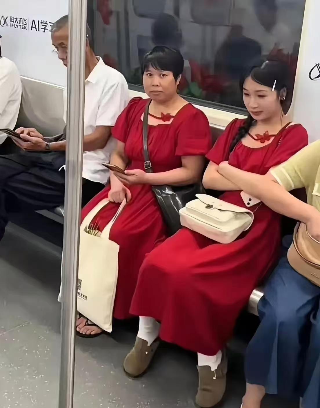 地铁上一位中年大妈穿着一条红裙，

哪知道与边上坐着的年轻女孩撞衫了，

只