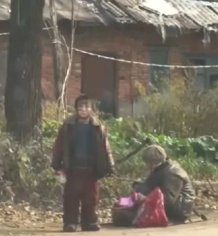 孩子脖子上栓着绳子，另一端在一位老人手中，老人挑着一桶泔水，两个人都脏乱不堪，交