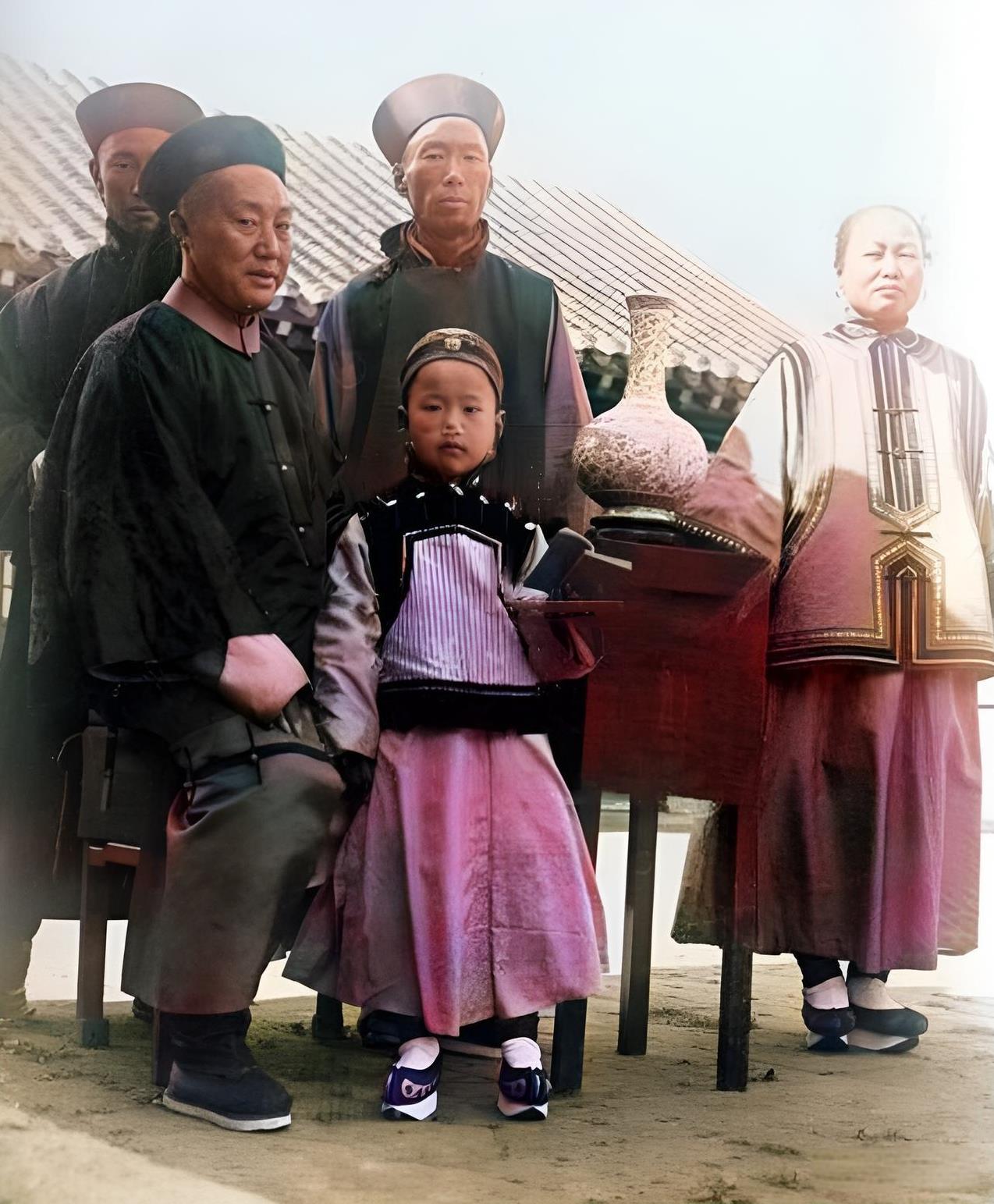 一八九七年，北京旗人官员与孩子和随从在院子里。这名官员头戴官帽，身穿官服，脚穿官