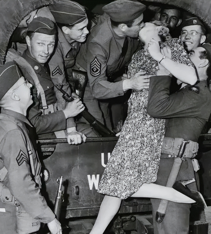 1940年，一名士兵举起一名年轻貌美的女人，将她送给卡车上的大兵，大兵见到女子不