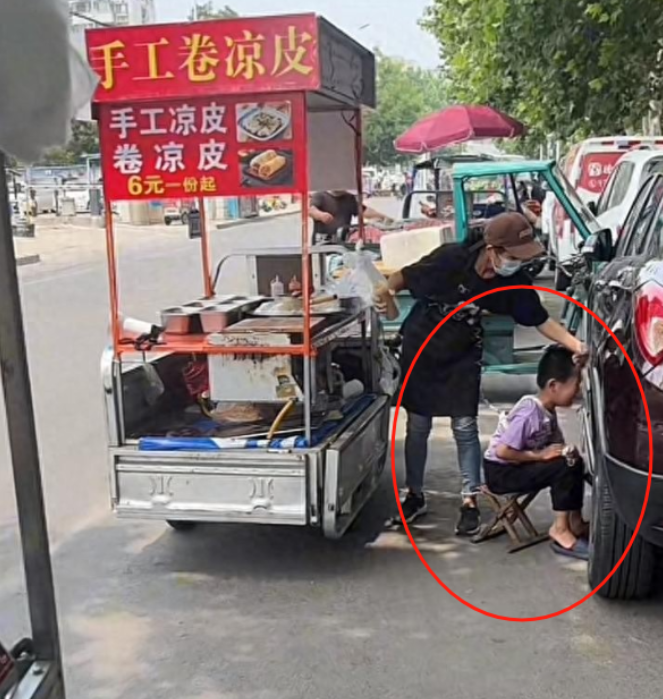 山东济宁，女子刘芳推着小车卖着凉皮，腰间用一根绳子拴着她患有自闭症的儿子小杰。这