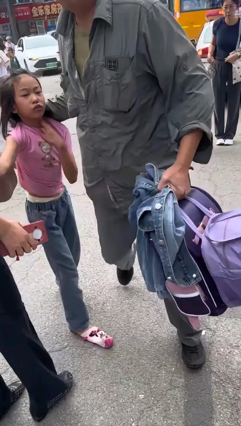 爷爷接孙女放学，可能孙女无理取闹了，爷爷劝说不听，爷爷强制提着孙女的后衣领前行，