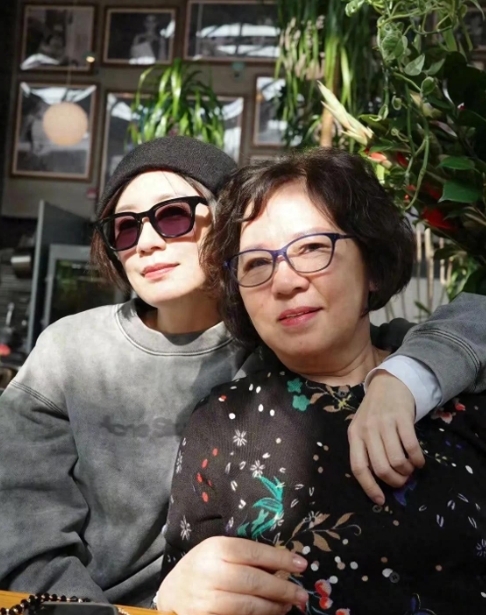 照片中，贾静雯身穿灰色卫衣，头戴黑色帽子，戴着墨镜，又美又飒，坐在她旁边的是贾妈