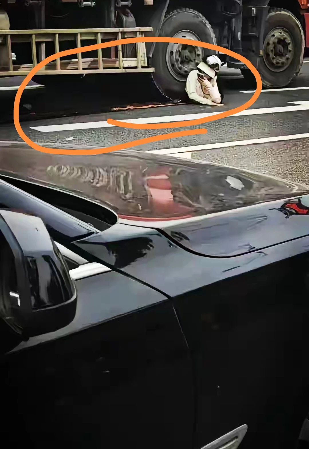 图片中一位女士被压在大货车车轮下，手里拿着手机，正在发语音，估计是遗言吧，可能她