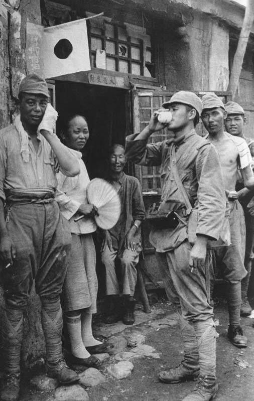 这张照片拍摄于抗战时期：四名日本士兵站在一户中国农家门前，门上悬挂着刺眼的日本国