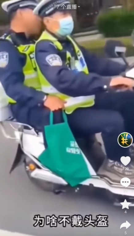 图片中有两个没戴头盔的交警正共骑着一辆电动车悠闲的在城市马路上快速行驶着。有位市