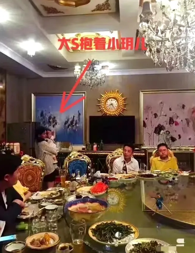 大s、汪小菲早年和朋友聚餐合影，汪小菲坐在饭桌上聊天喝酒，大s站在旁边抱着女儿。