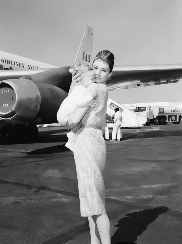 1961年，赫本抱着一岁的儿子肖恩准备登机。镜头下的她身着长裙，气质尊贵优雅、落