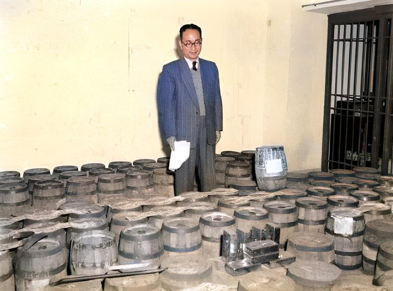 1949年，一名戴着眼镜、西装革履的男子检查登记一桶桶的黄金。这些木桶的里的黄金