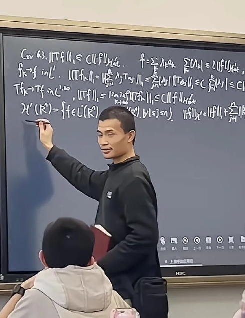 韦东奕，右手拿着笔，站在讲台上，在北大给学生们上数学课，密密麻麻写了一黑板。
