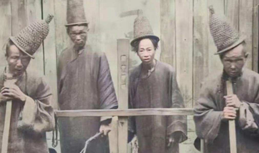 这是一张拍摄于清朝福建古田县的衙役照片。画面中四位着长衫的衙役站在木板墙前，他们