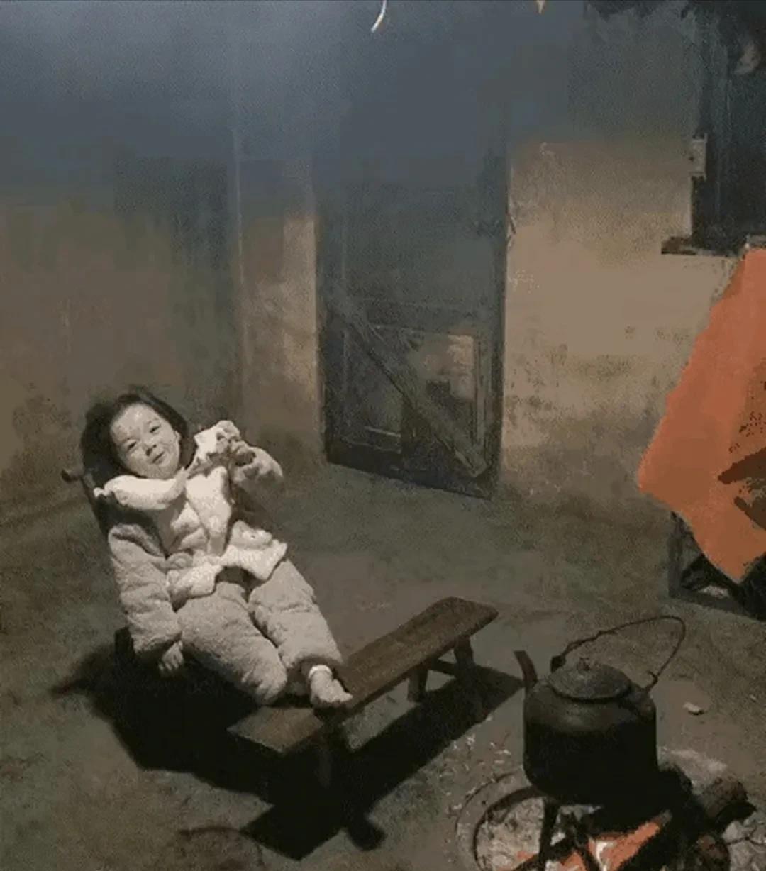 看到小女孩在农村姥姥家的场景，心被触动了。她稳稳坐于板凳，手握烤番薯，身旁小火炉