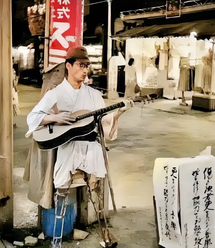 这是战后日本的街头，一名在战争中失去双腿的日本老兵，抱着吉他，弹唱乞讨。他头戴军