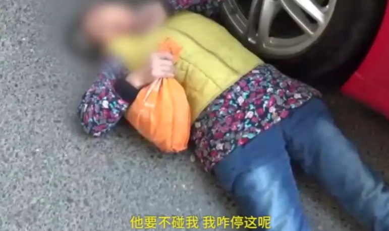 2022年辽宁沈阳，大妈看见路边停放了一辆好车，用身体蹭上车灯，然后就躺在车前面