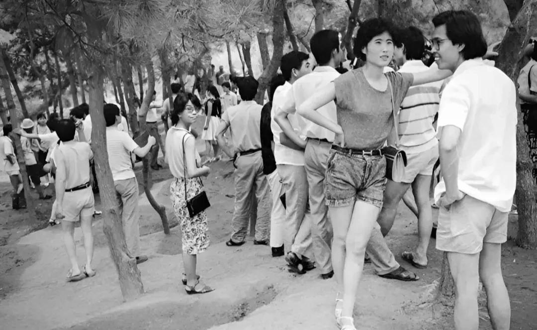 80年代，正在户外一角热情交流的青年男女，从穿着来看，个个都是那个时代的时尚弄潮