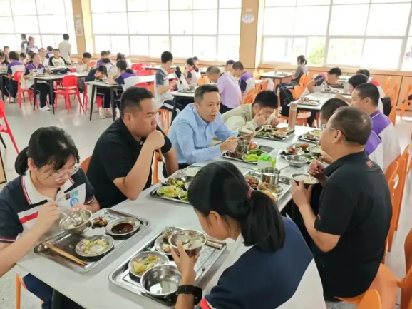 下面这张照片反映的是某地级市教育局长到所属县一所中学检查工作，并与学生一起就餐的