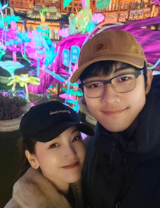 照片中，金莎穿着白色的皮草外套，和小19岁男友孙丞潇同框合影秀恩爱，嘟嘴卖萌好可